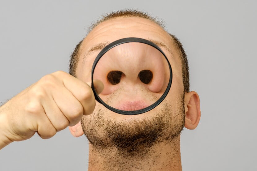 Man holding magnifying glass to his nose